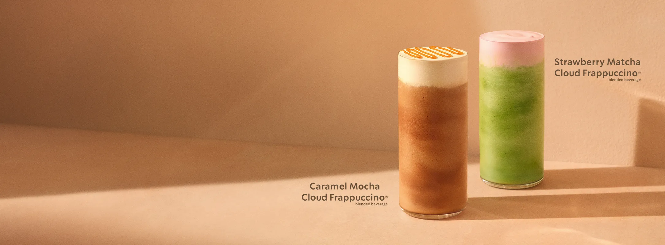 Two tall blended Starbucks Cloud Frappuccino beverages on a warm beige surface. On the left a Caramel Mocha Cloud Frappuccino with a light foam top and caramel drizzle, on the right a Strawberry Matcha Cloud Frappuccino with vibrant green blended matcha and a pale pink foam layer.