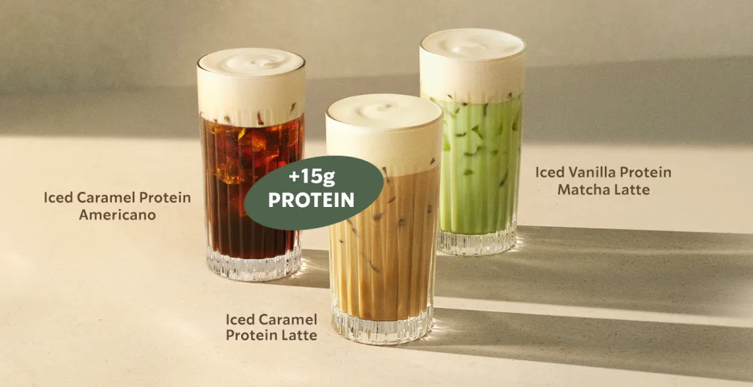 Three iced drinks topped with thick, creamy protein cold foam are displayed on a light surface. 