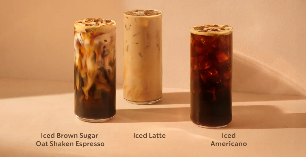 Three iced Starbucks drinks displayed on a warm beige background. From left to right: an Iced Brown Sugar Oat Shaken Espresso with swirling layers, an Iced Latte with ice throughout, and an Iced Americano with dark coffee and ice cubes.